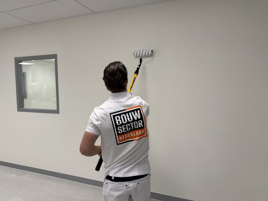 Schilder van Bouwsector Nederland saust een witte muur met een grijze plint en een binnenraam