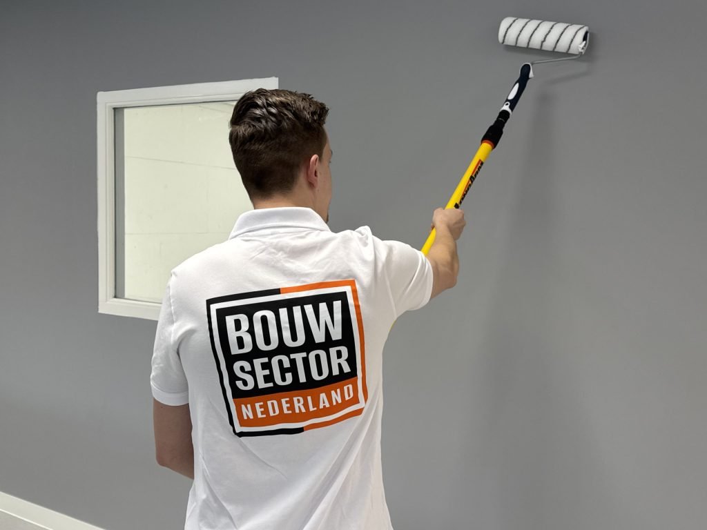 Schilder van Bouwsector Nederland zet een grijze muur in de verf naast een wit kozijn