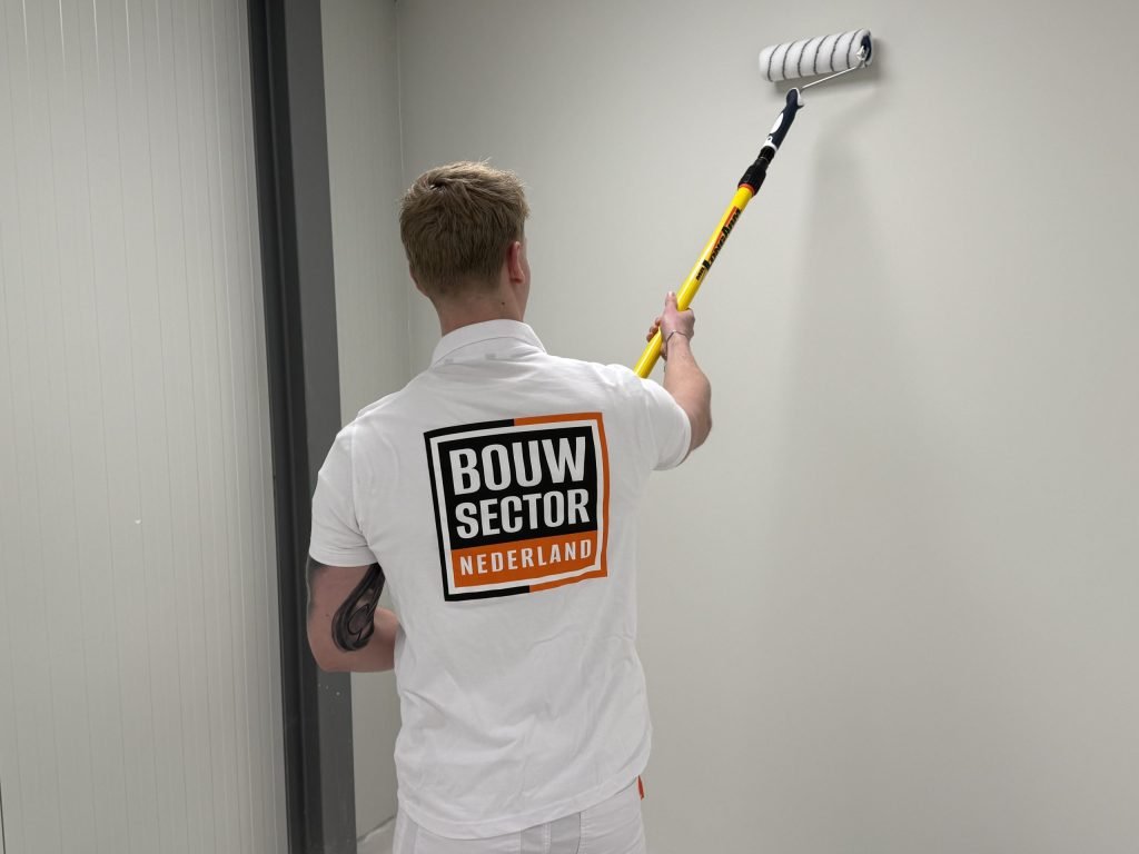 Schilder van Bouwsector Nederland rolt een lichte wand in een smalle gang