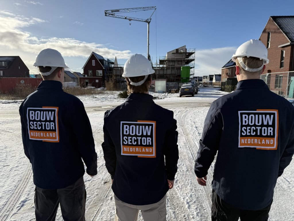 Drie collega's van Bouwsector Nederland met witte helm en logo op de rug kijken naar een nieuwbouwstraat in de sneeuw